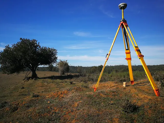 Antena GNSS sobre trípode en terreno abierto, con un árbol al fondo