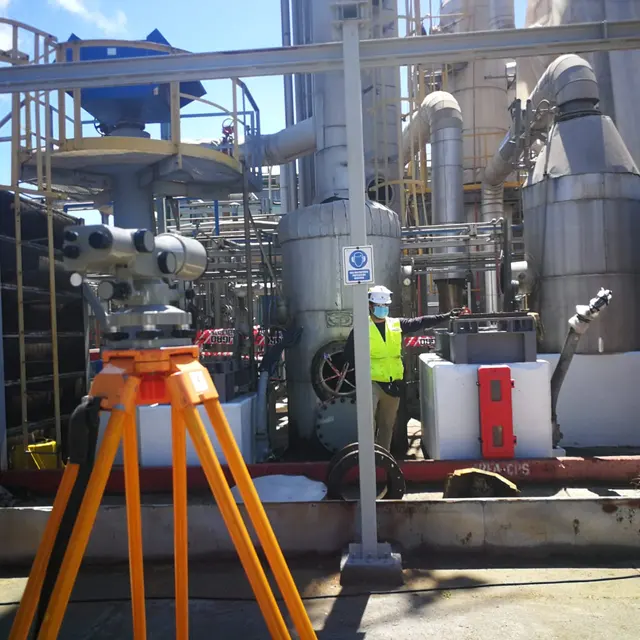 Topógrafo con nivel óptico sobre trípode en una planta industrial