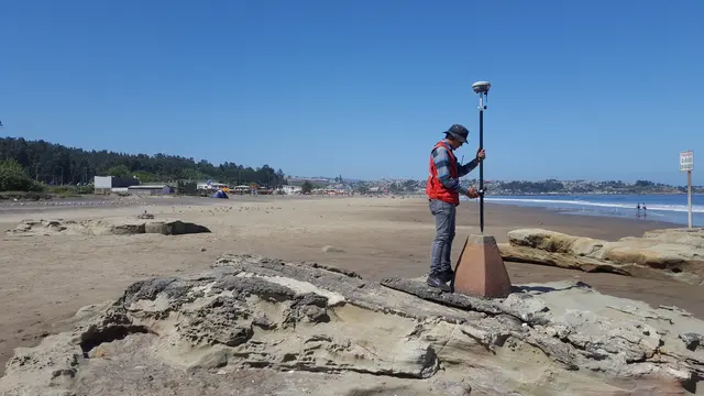 Técnico midiendo con antena GNSS sobre un mojón en una playa